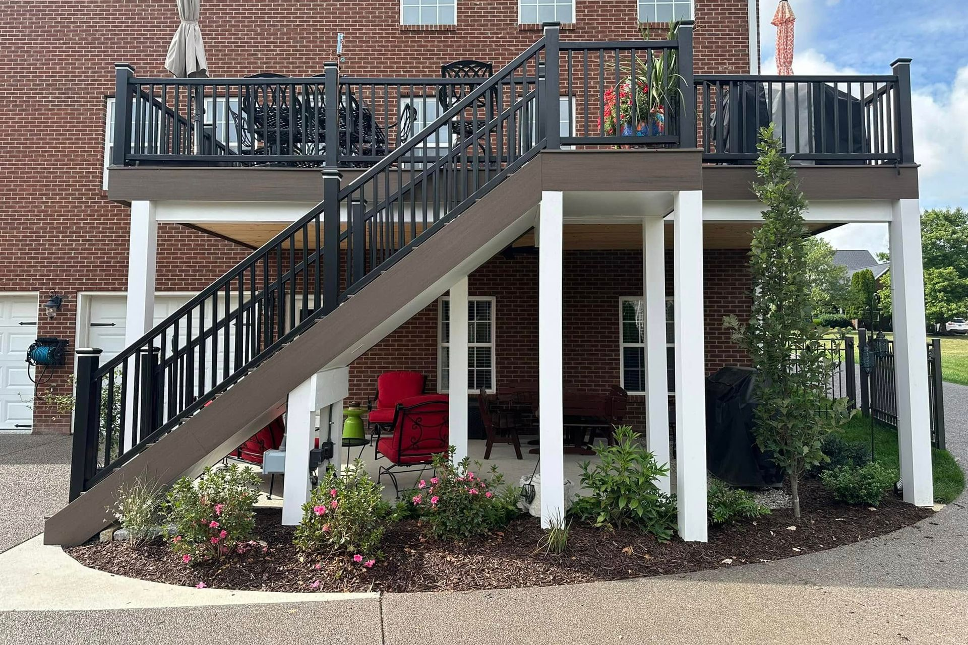 Multi-level deck with stairs; black railing, brown decking, white support posts, brick building.