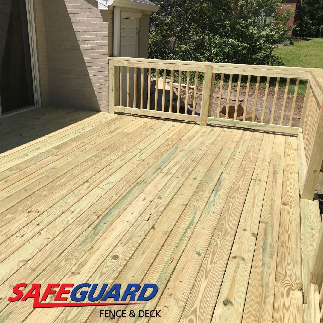 Wooden deck with railing. Light brown wood, green tinge. House in the background. 