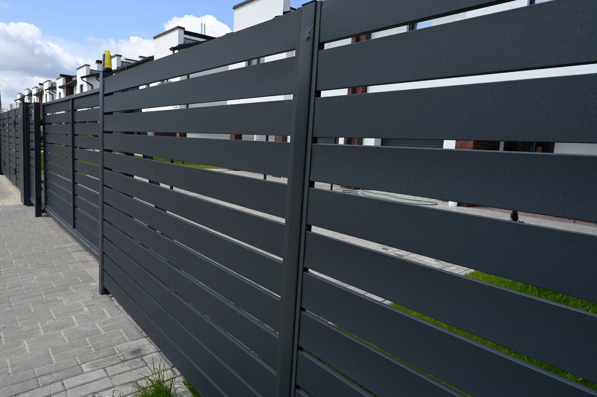 Dark gray horizontal slat fence along a sidewalk.