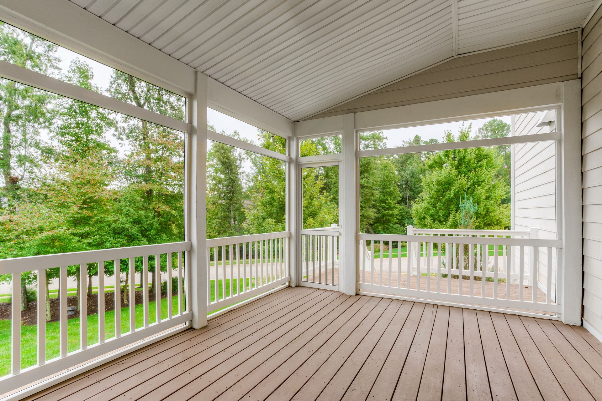 Covered porch with white railings and screen overlooking a green yard and trees.