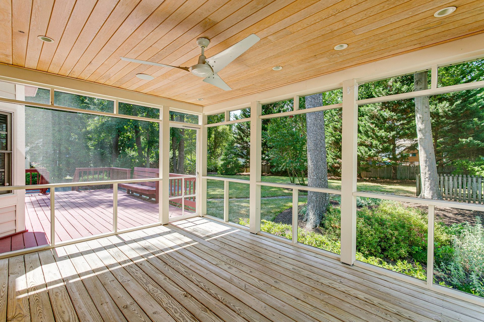 Screened porch with wooden floor and ceiling, looking out at a backyard with trees.