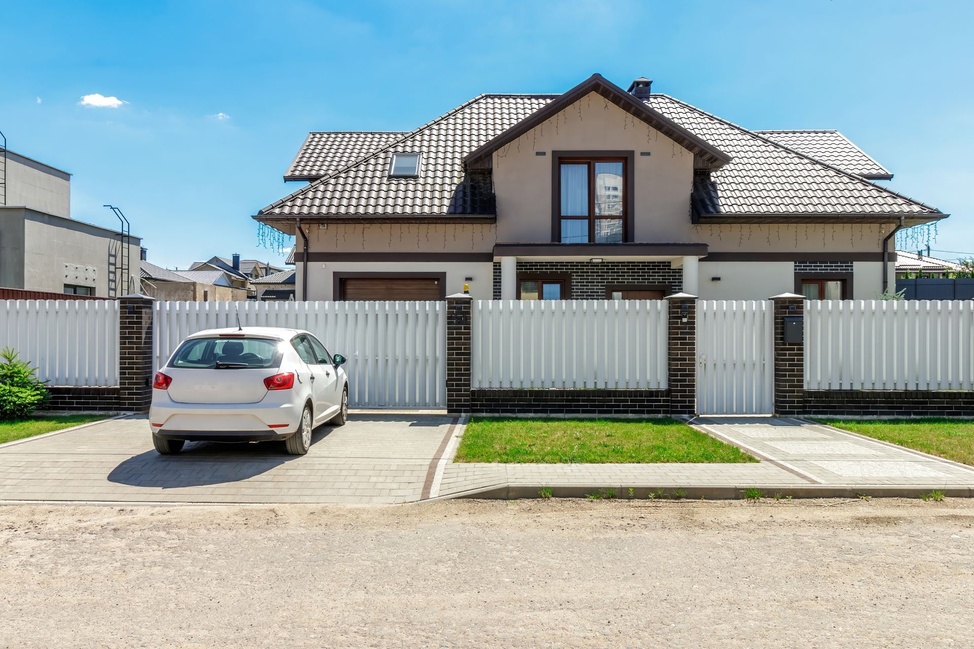 White car parked in front of a beige house with a white fence on a sunny day.