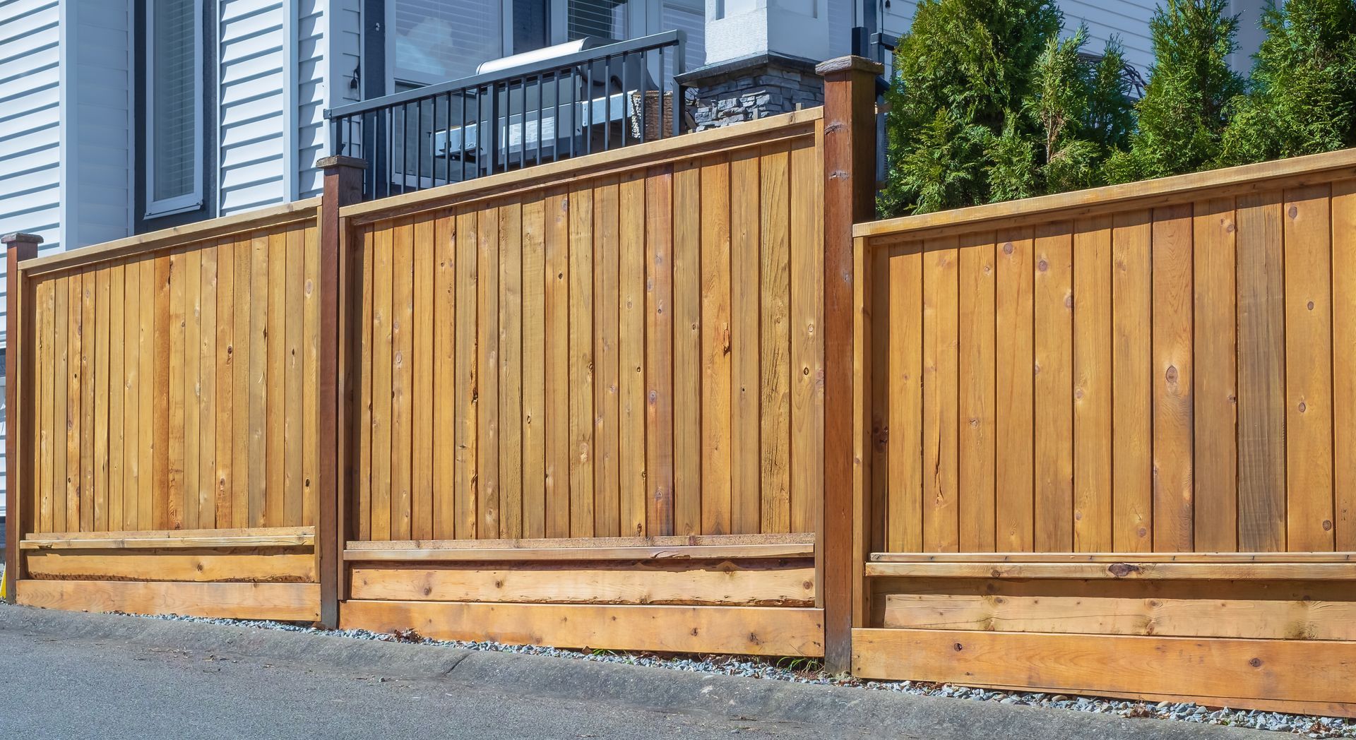 Wooden privacy fence along a gravel driveway beside a house with blue siding
