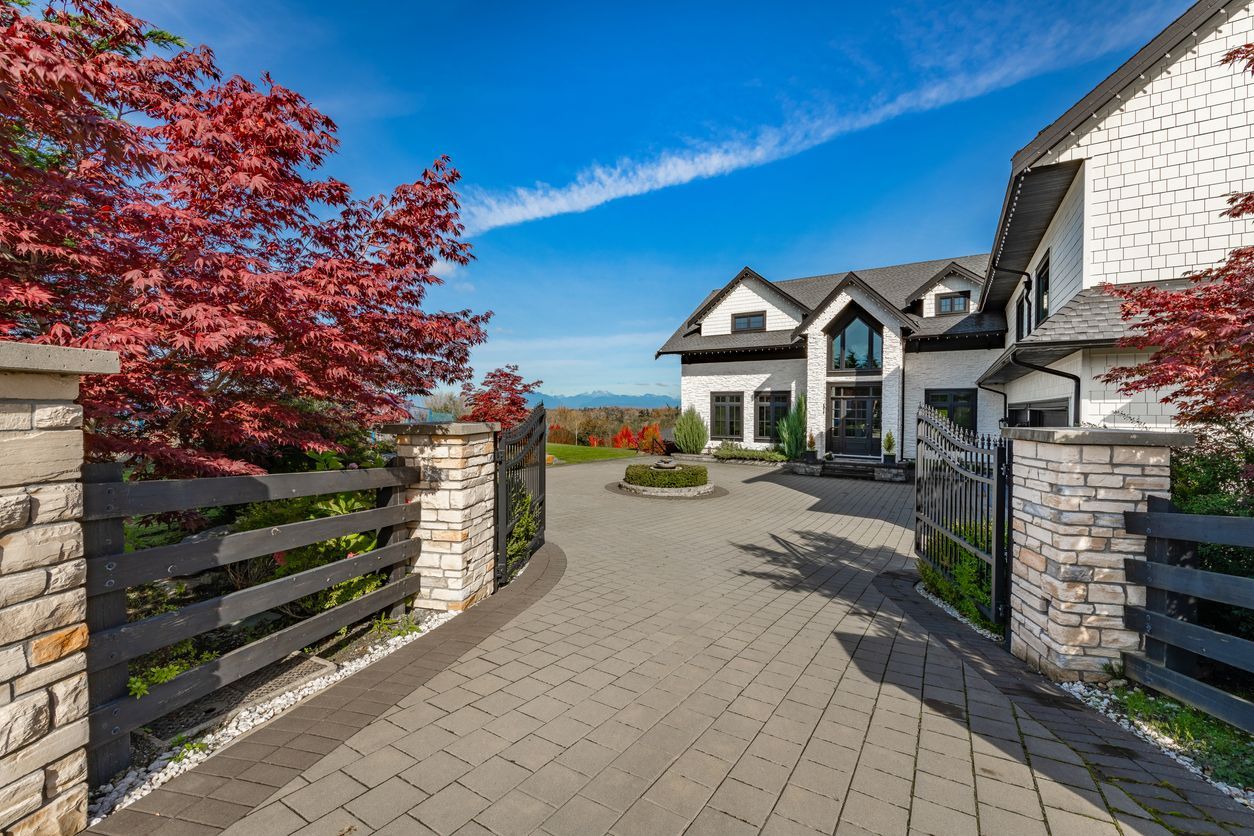 Elegant white house with black trim, driveway, and autumn foliage under a blue sky.