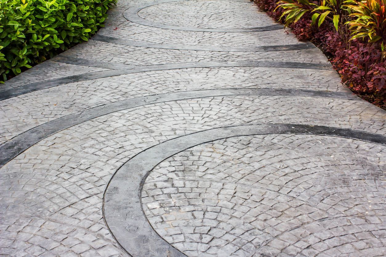 Curved cobblestone path with dark gray borders, lined by green and red-burgundy shrubs.