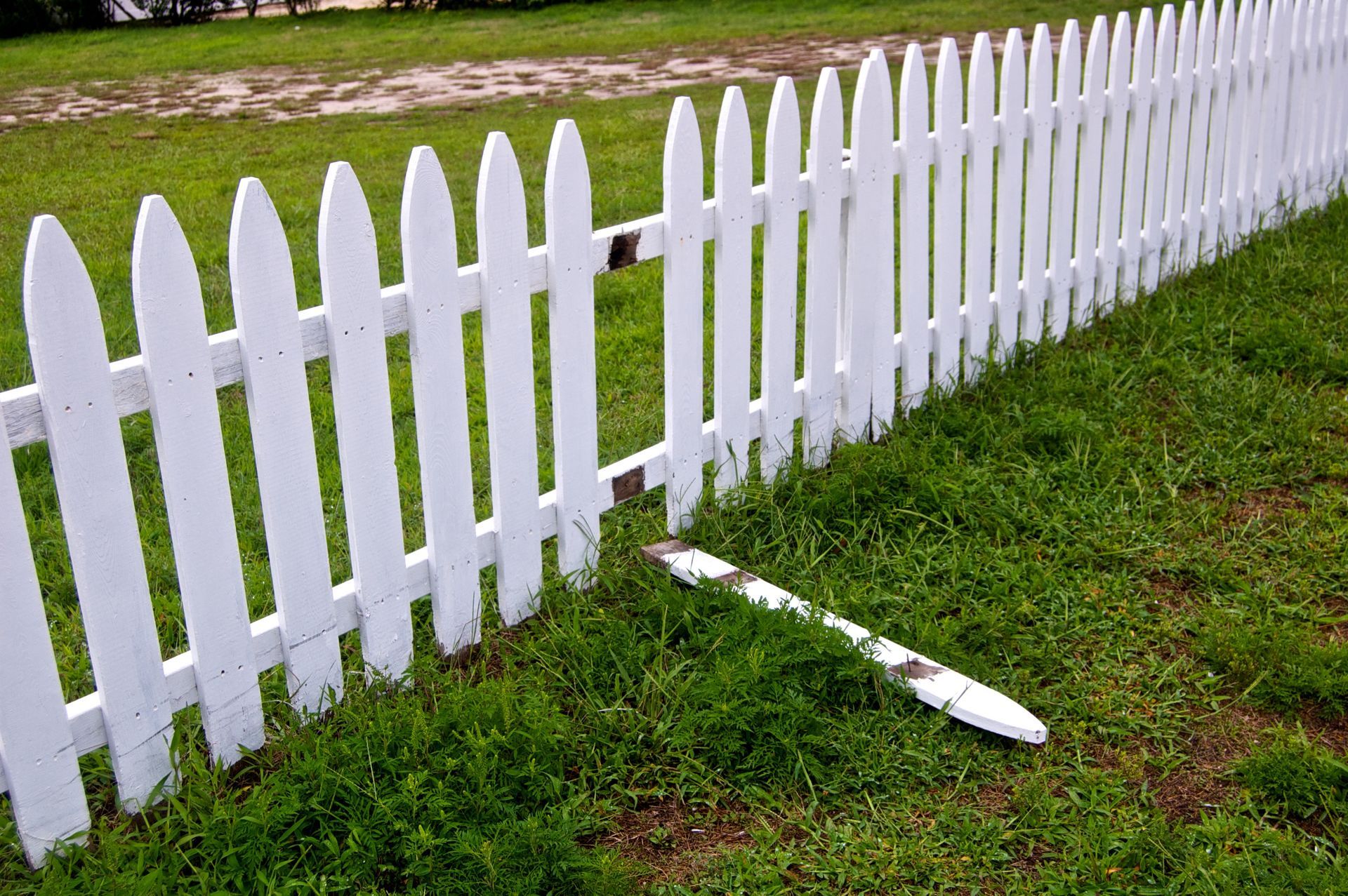 Broken white picket fence in a grassy yard with one fallen panel