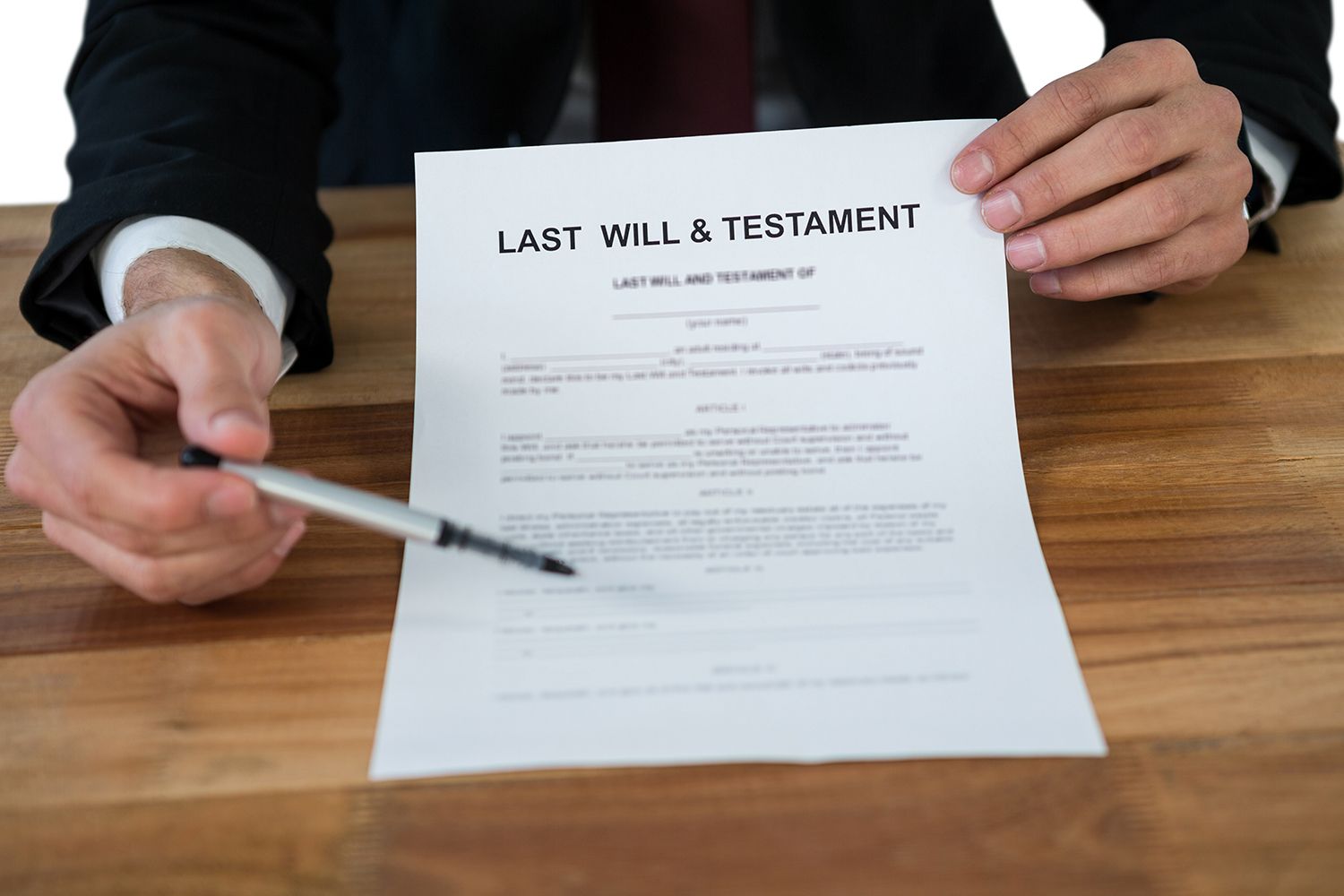 Person in suit pointing a pen at a Last Will & Testament document on a wooden table. Person in suit pointing a pen at a Last Will & Testament document on a wooden table.