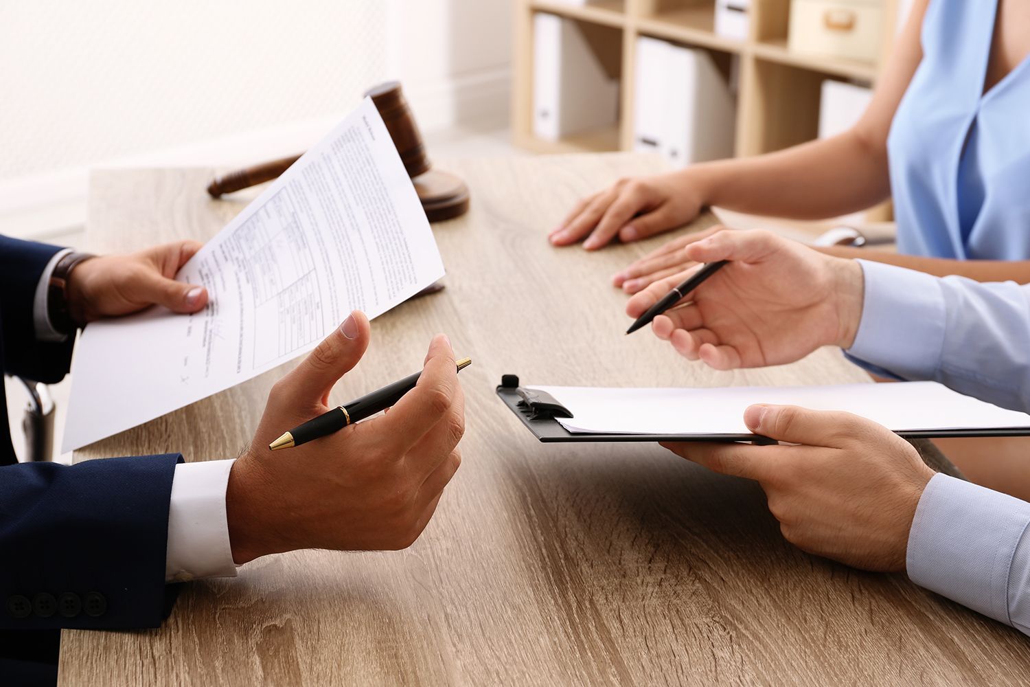People reviewing documents at a wooden table, one person holding a pen, gavel in the background. People reviewing documents at a wooden table, one person holding a pen, gavel in the background.