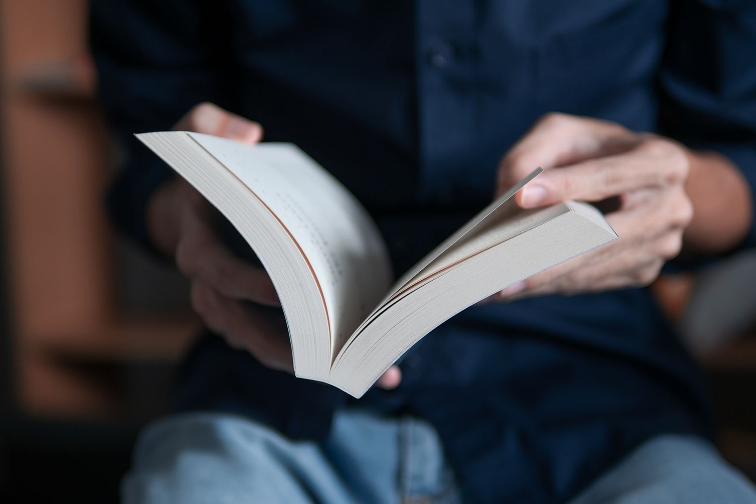 Person in a blue shirt and jeans reading a book, holding it open. Person in a blue shirt and jeans reading a book, holding it open.