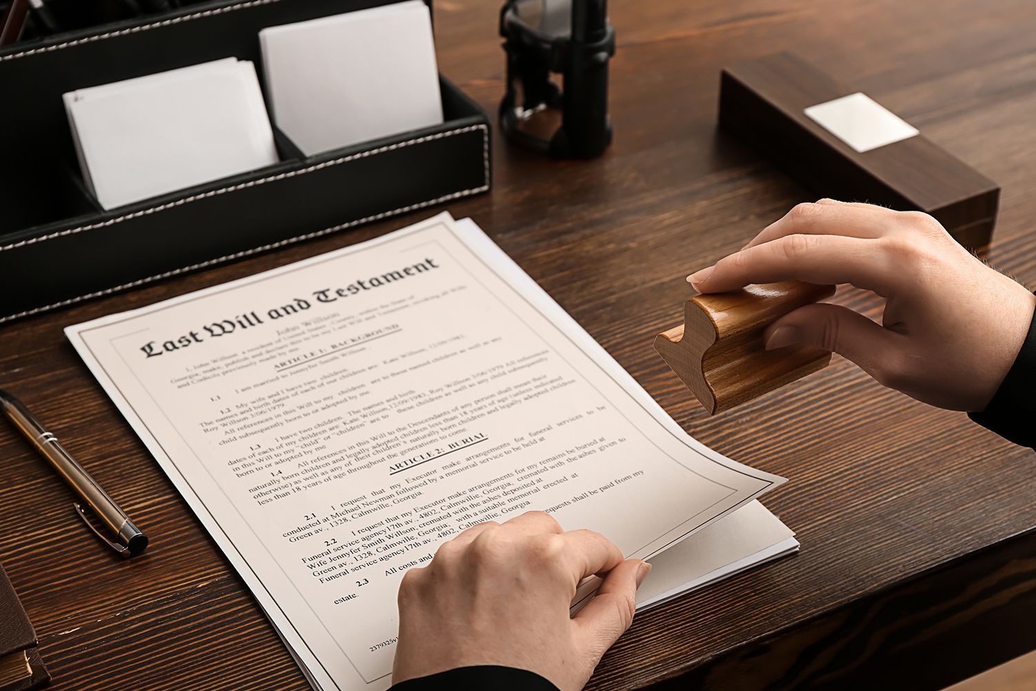 Person signing Last Will and Testament document with a stamp on a wooden desk. Person signing Last Will and Testament document with a stamp on a wooden desk.