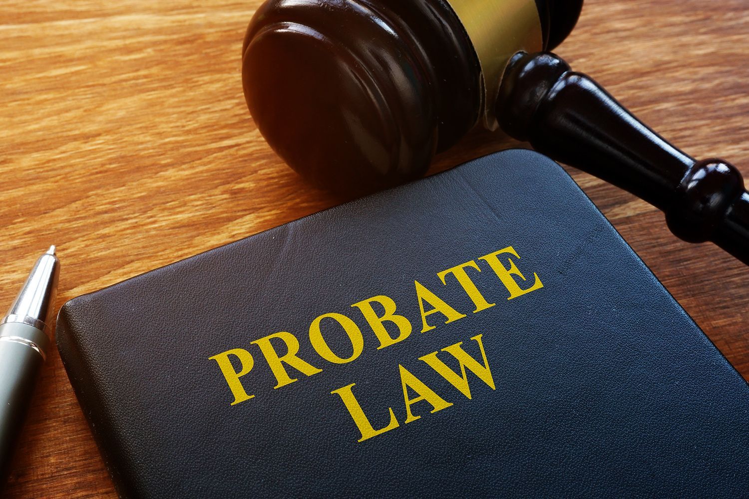 Close-up of a blue book titled PROBATE LAW with a gavel and pen on a wooden surface. Close-up of a blue book titled PROBATE LAW with a gavel and pen on a wooden surface.