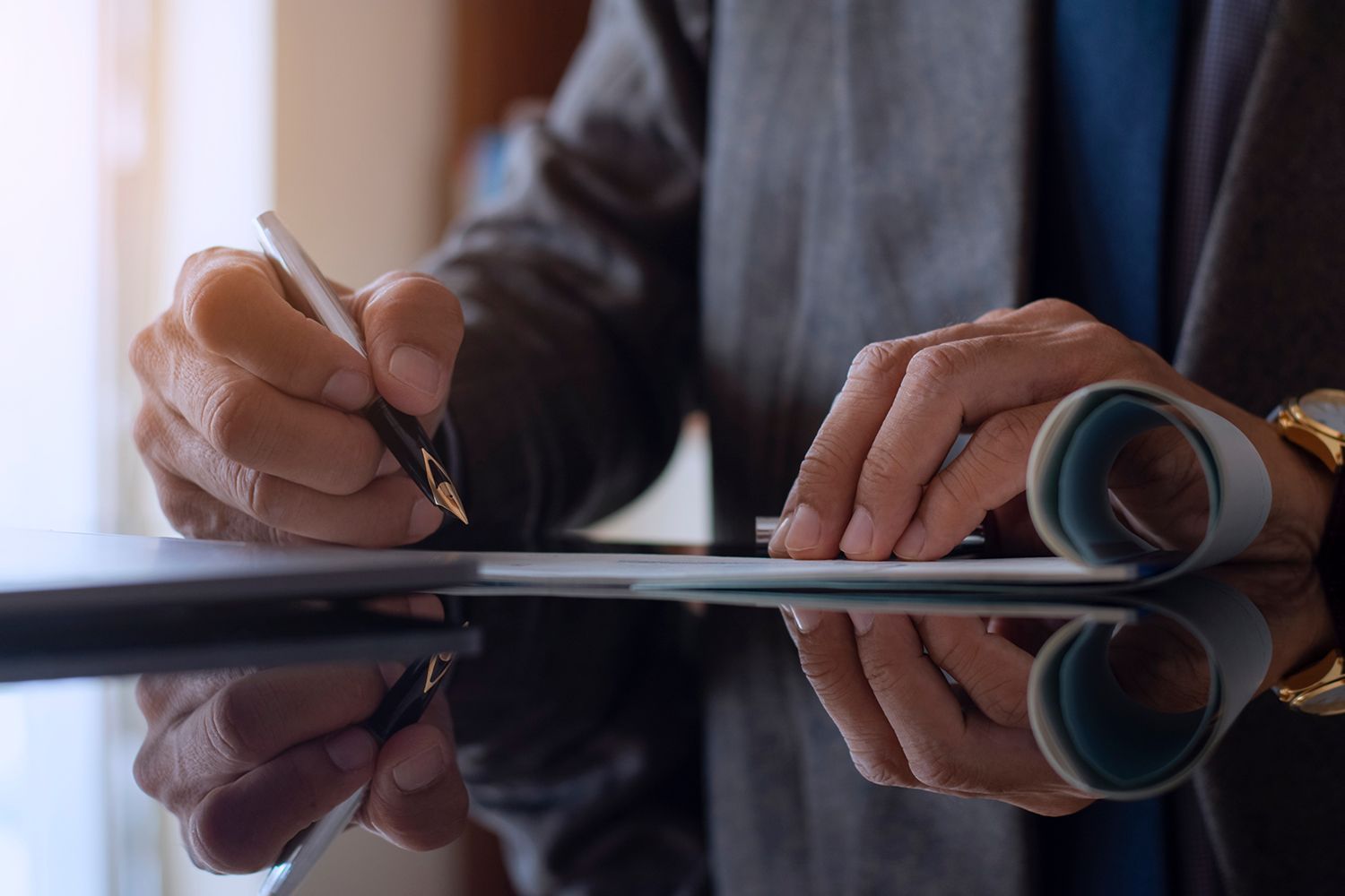 Person signing a document with a pen, close-up. Table with reflections, watch on wrist. Person signing a document with a pen, close-up. Table with reflections, watch on wrist.