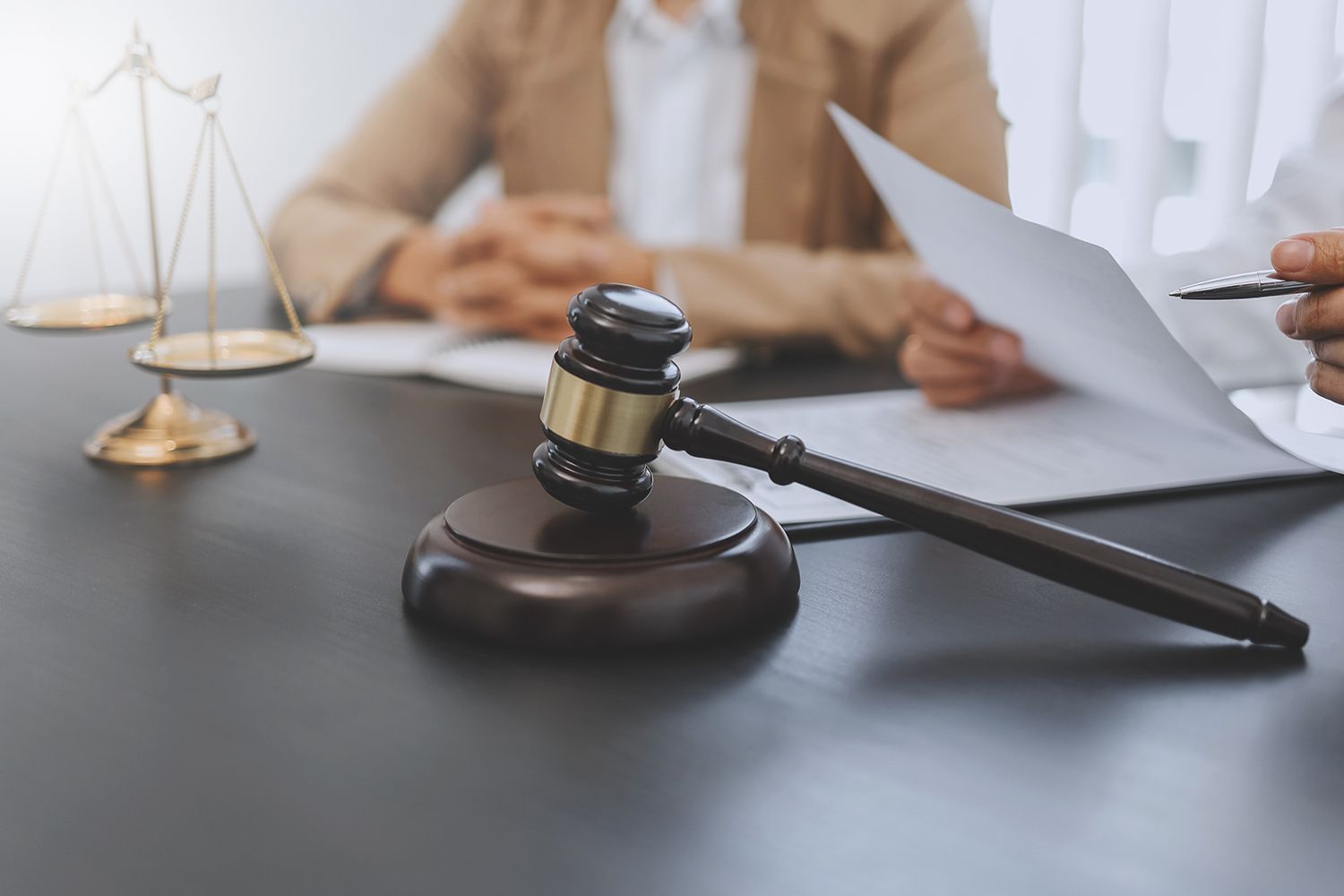 Gavel on a table with scales of justice and people reviewing documents.