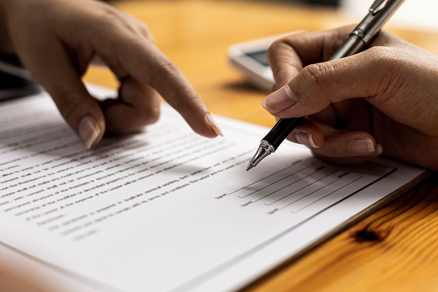 Hands pointing to a document as another hand signs it with a pen.