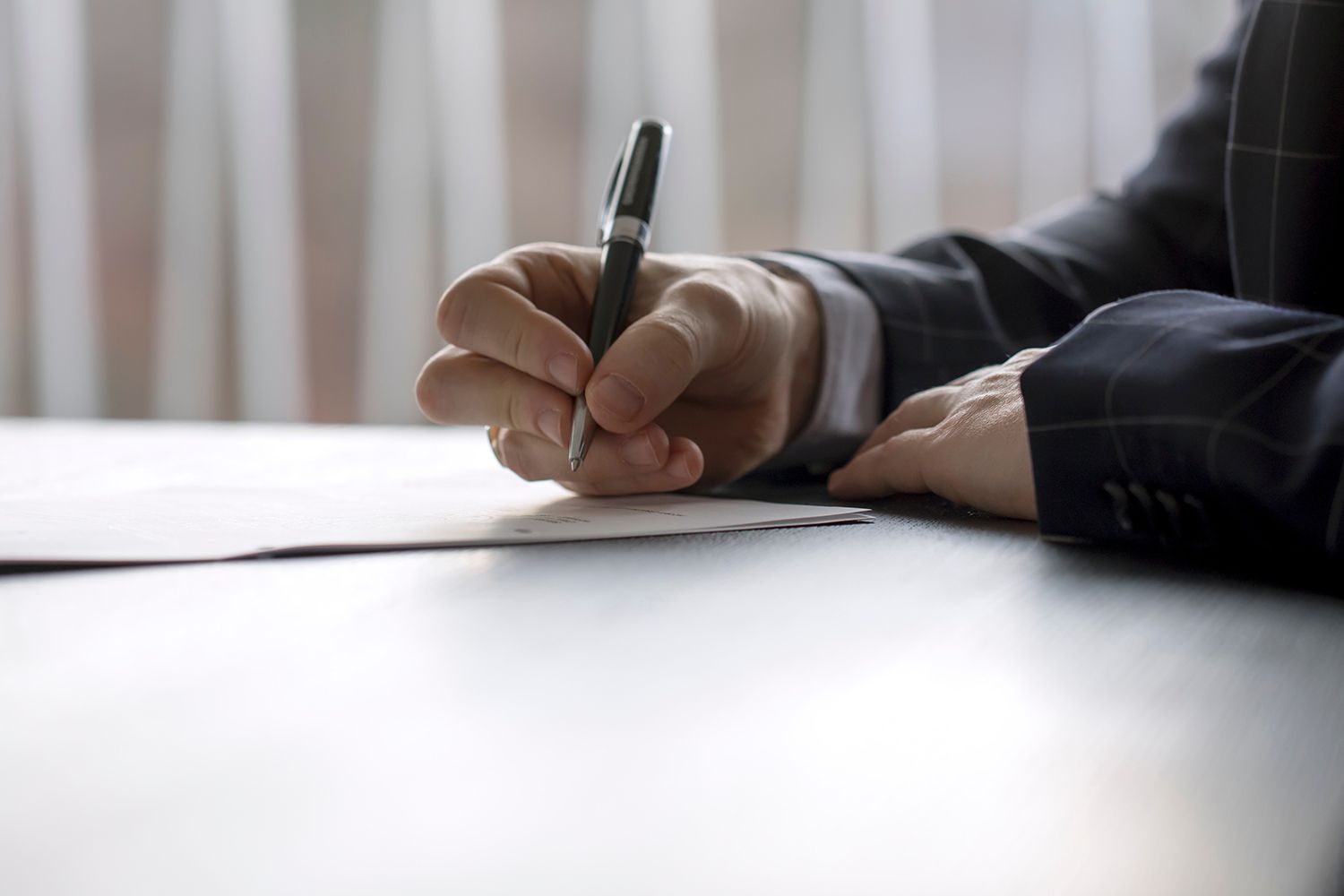 Person in suit writing with pen on a white paper at a table. Person in suit writing with pen on a white paper at a table.
