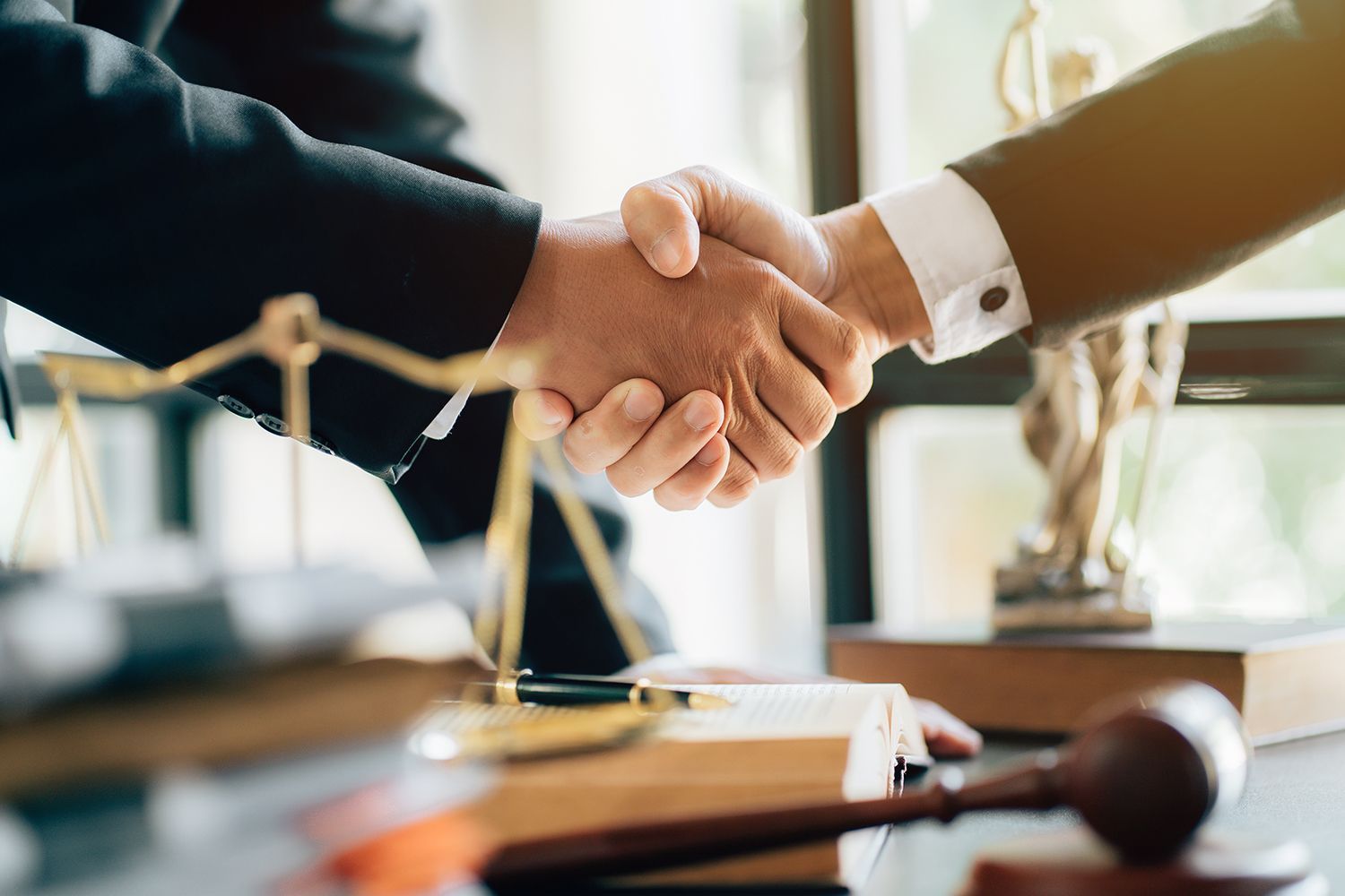Two people shaking hands near legal symbols, suggesting a deal or agreement.