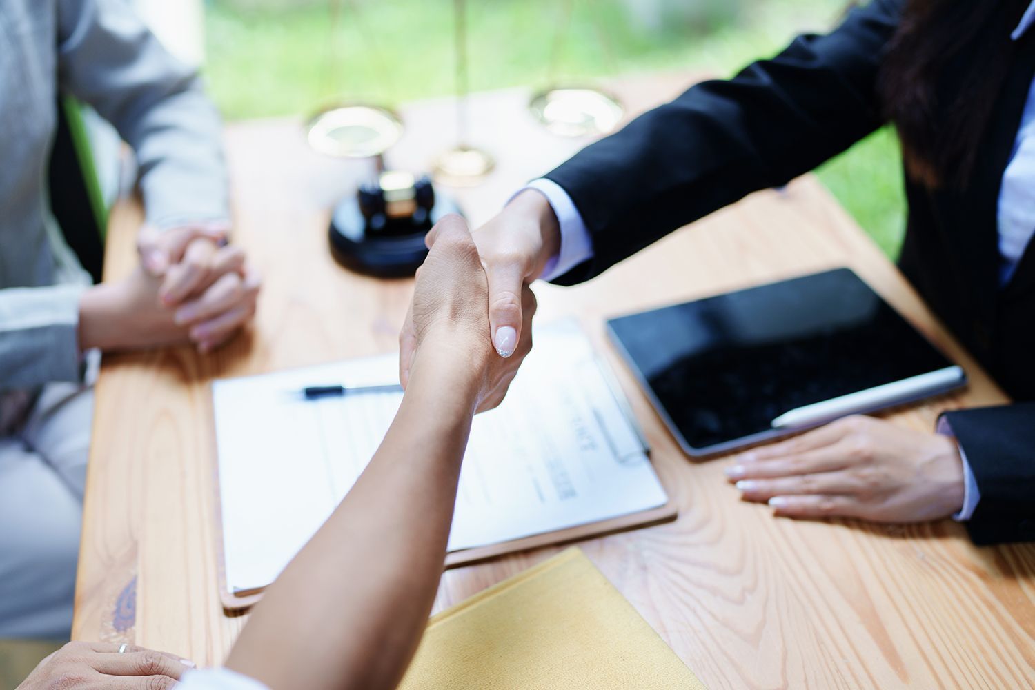 Two people shaking hands over a desk with documents and a tablet. Two people shaking hands over a desk with documents and a tablet.