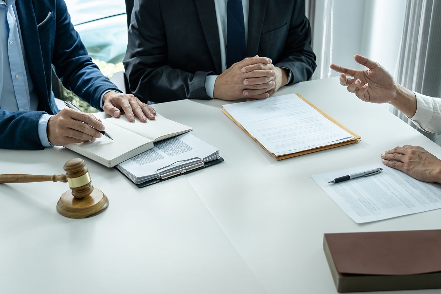 Three people in suits at a table with documents, a gavel, and a notepad. Someone gestures. Three people in suits at a table with documents, a gavel, and a notepad. Someone gestures.