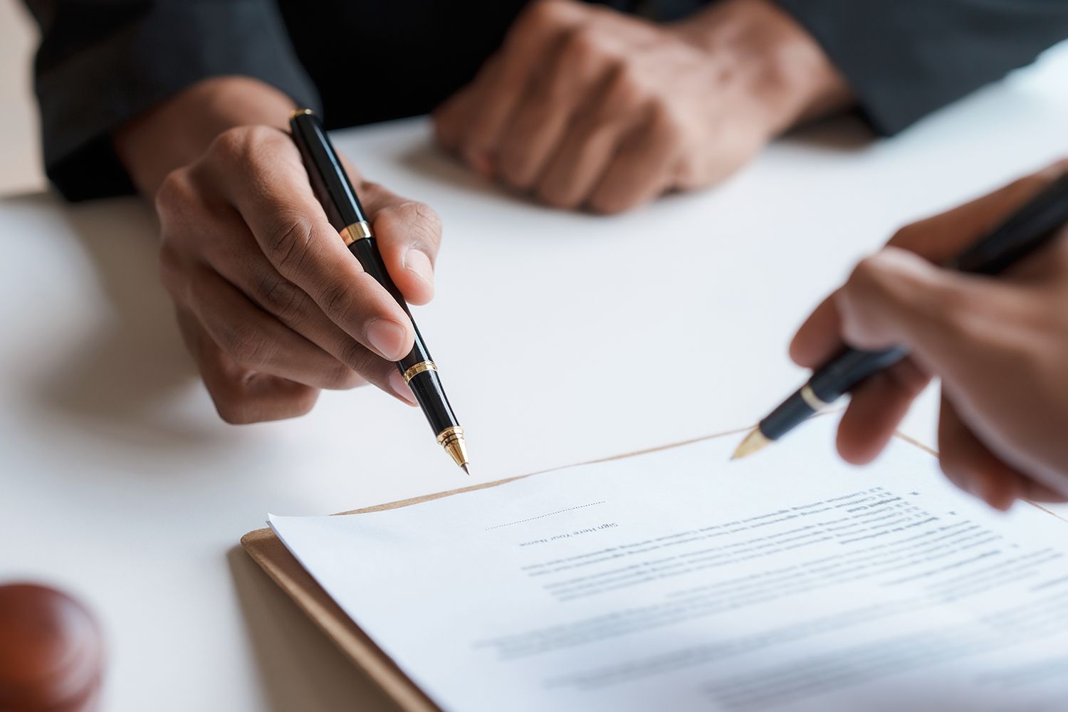 Hands holding pens, pointing at a document on a clipboard.