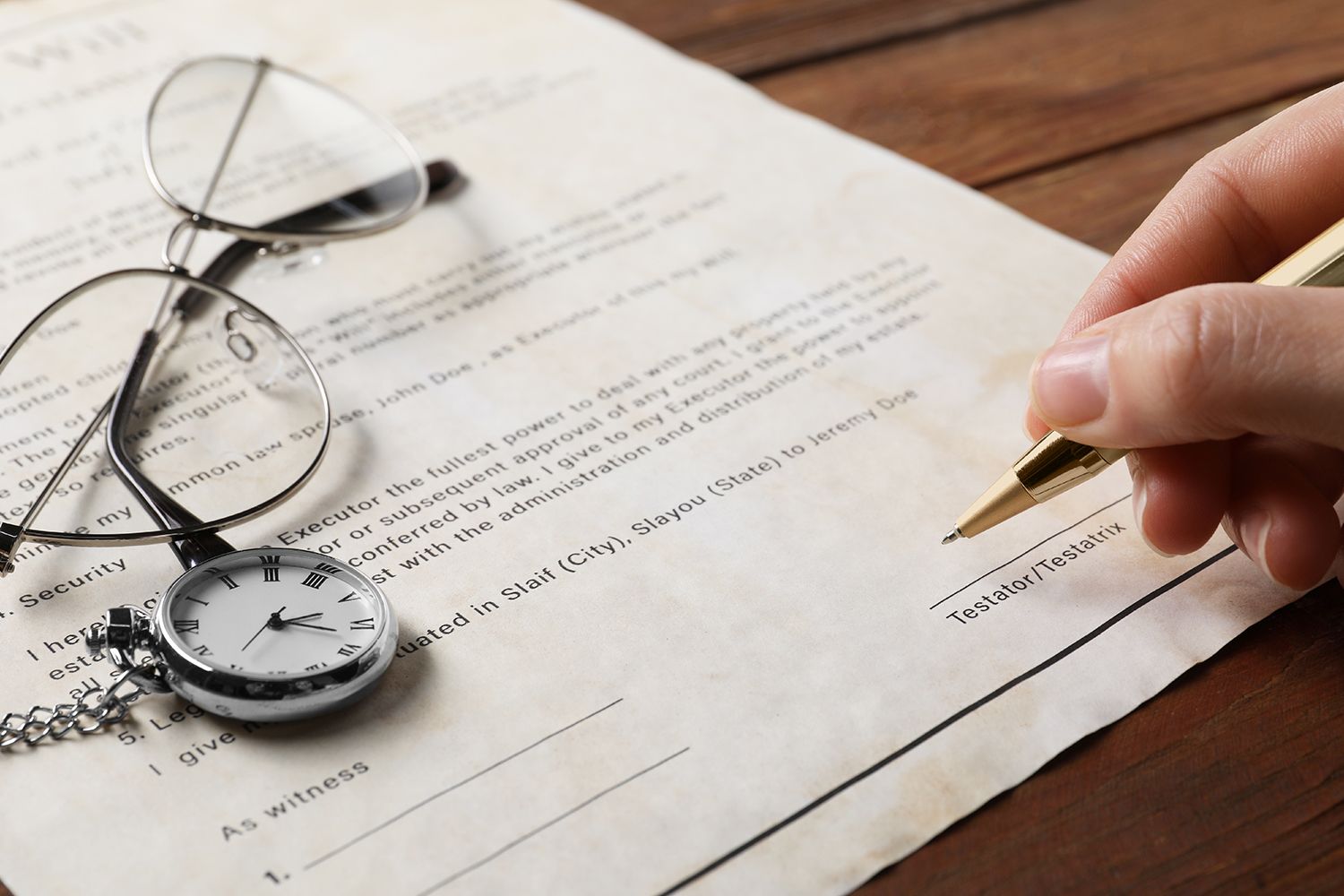 Hand signing document with pen, beside glasses and pocket watch. Hand signing document with pen, beside glasses and pocket watch.