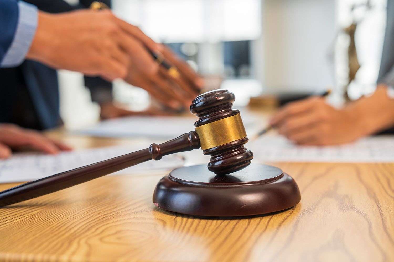 Gavel on wooden table with people blurred in the background, possibly in a courtroom. Gavel on wooden table with people blurred in the background, possibly in a courtroom.