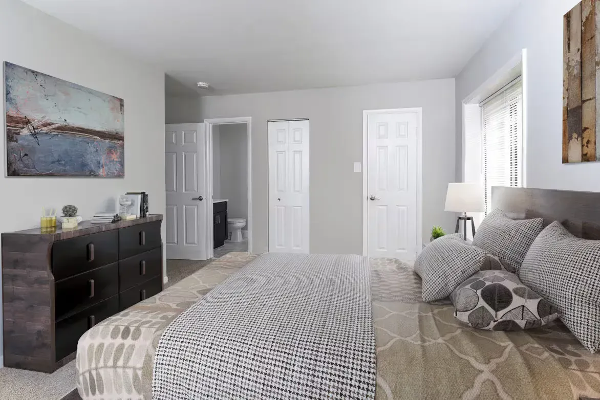 Bedroom in a modern apartment: large bed, dresser, and doorway to a bathroom.