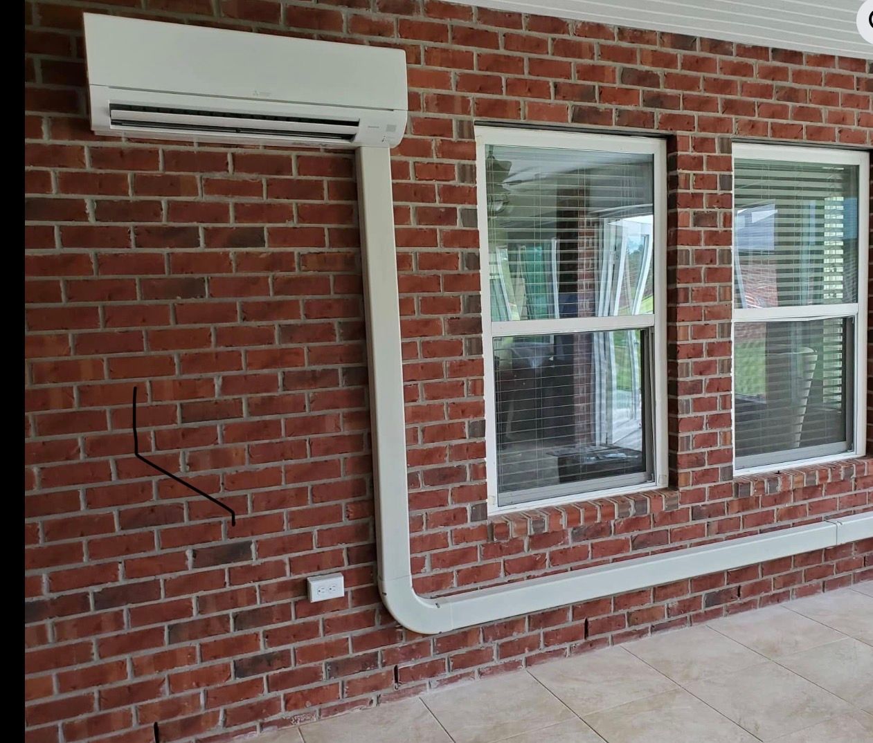 Brick wall with a wall-mounted air conditioner, two windows, and a visible crack near the floor.