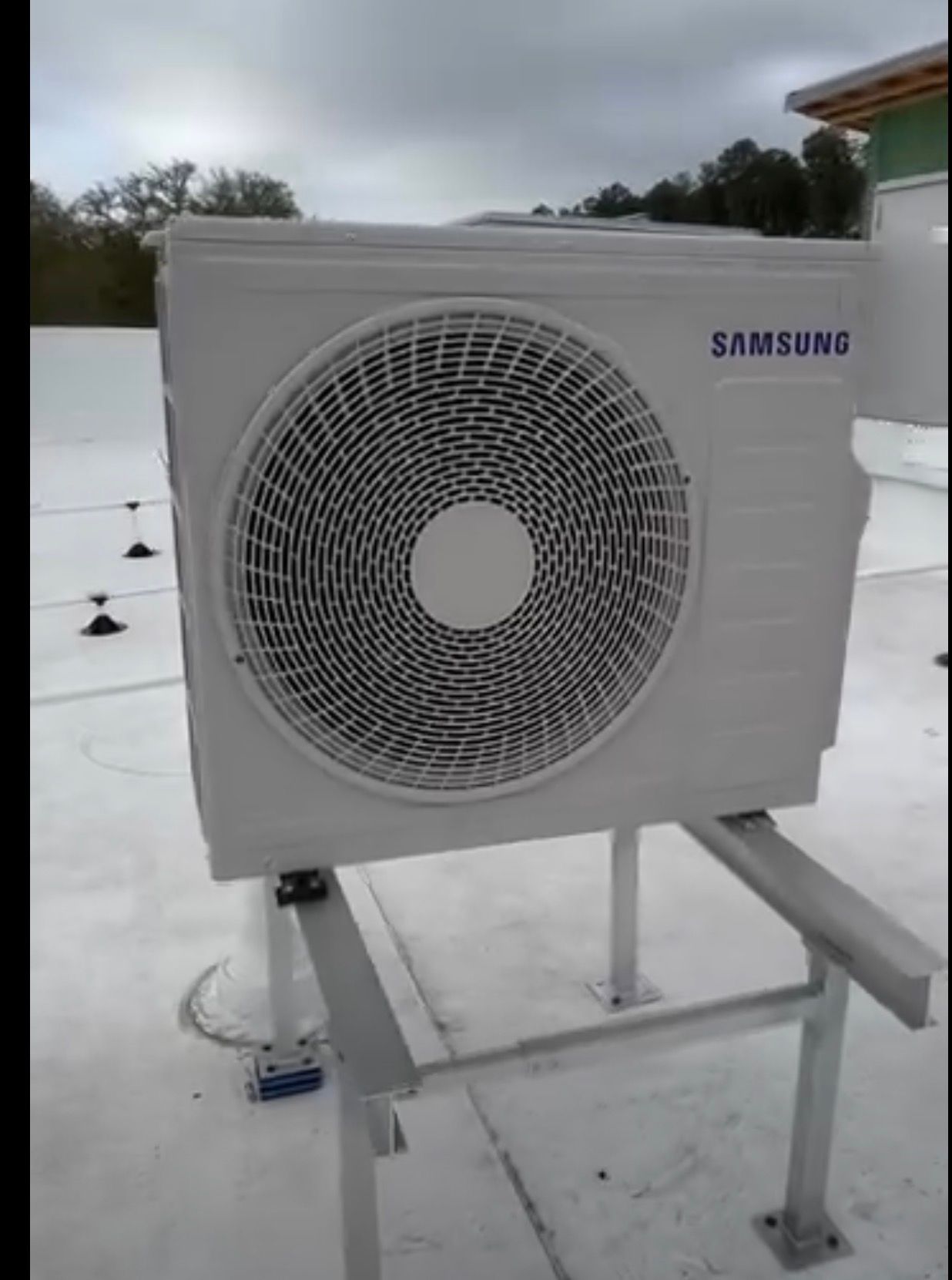 Samsung outdoor air conditioning unit on a snowy rooftop, with a large circular fan grille.