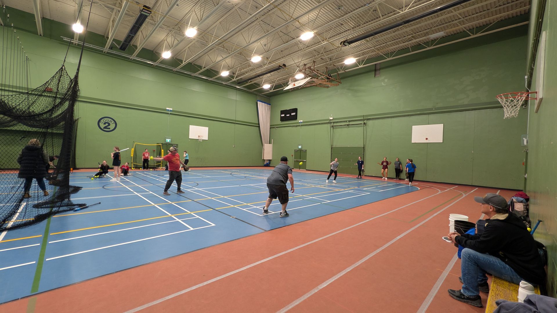 People practice pickleball on an indoor multi-sport court with blue flooring and a surrounding red track.