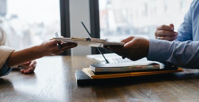 person passing a signed document to someone else across a desk