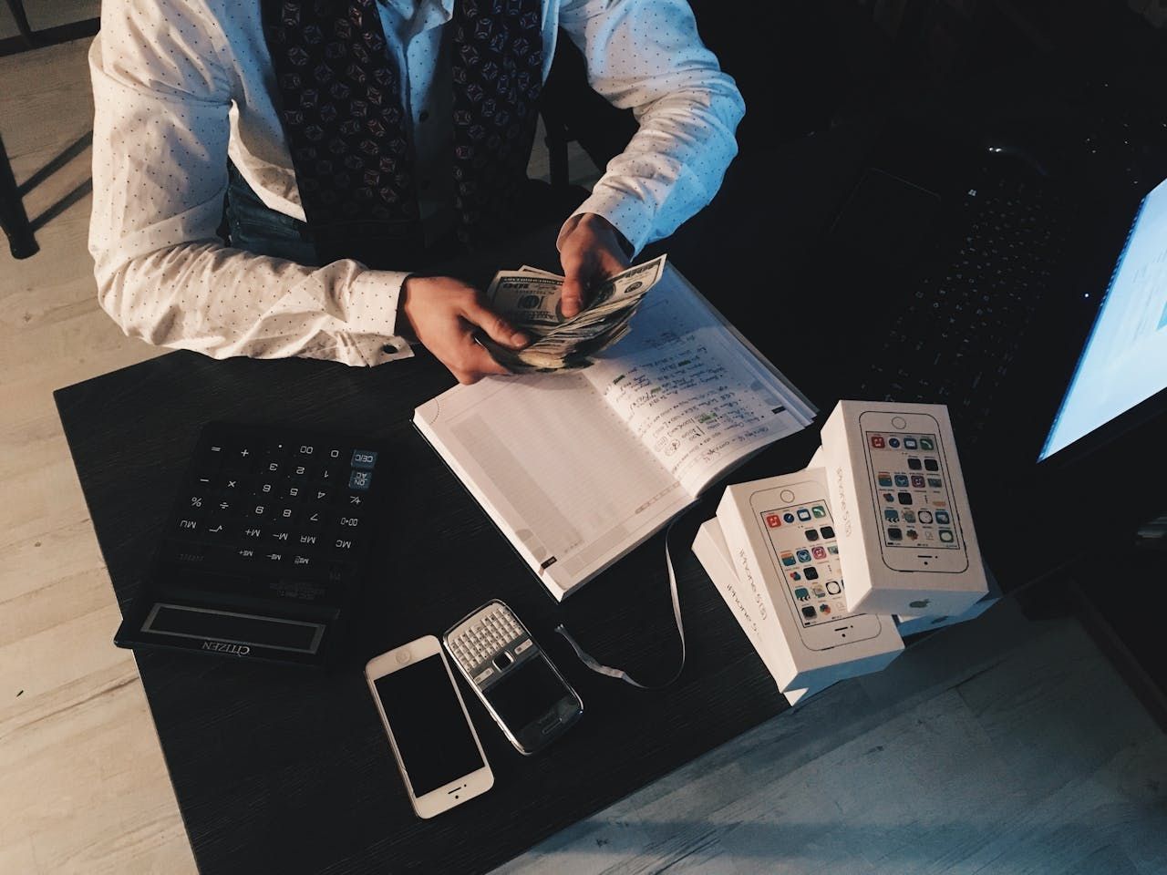 person counting money with papers and phones on desk