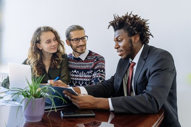 three people sitting at a table discussing something on a clipboard