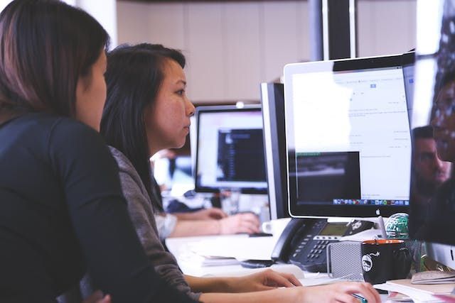two people looking at multiple monitors as they work