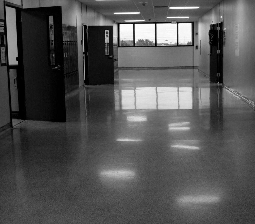 Empty school hallway with lockers, windows, and a polished floor reflecting ceiling lights.