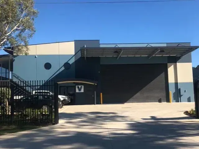 Industrial warehouse exterior with black roller door, beige walls, and a sunny driveway entrance