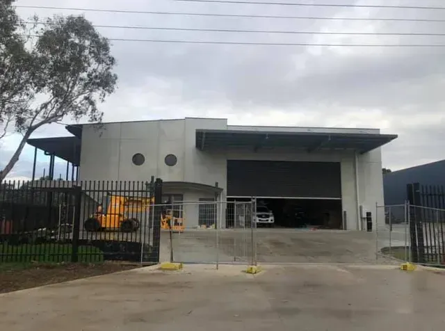 Industrial building with a gated entrance and yellow machinery under a cloudy sky
