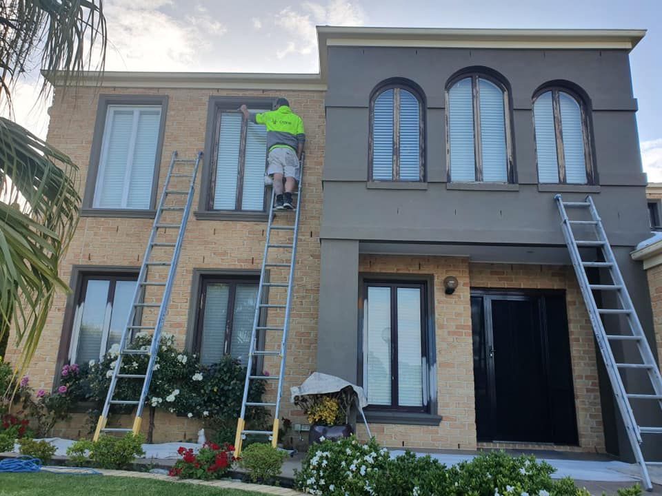 Two-story house exterior with ladders and a worker painting the upper wall