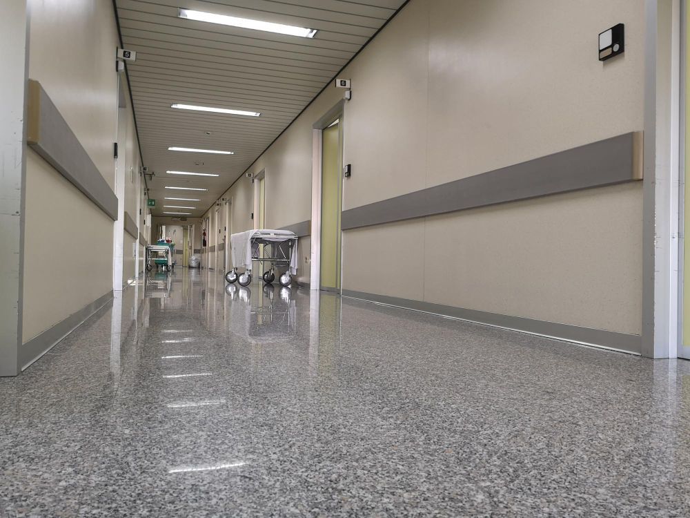 Empty hospital corridor with polished floor, beige walls, and overhead fluorescent lights
