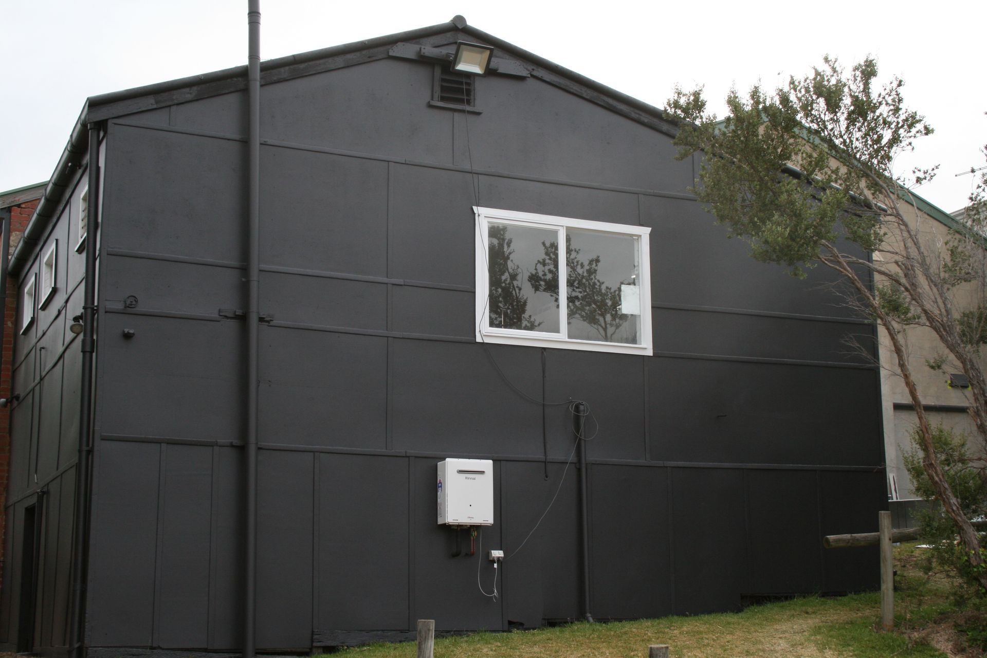 Dark gray two-story house exterior with a small white window and utility box on the wall