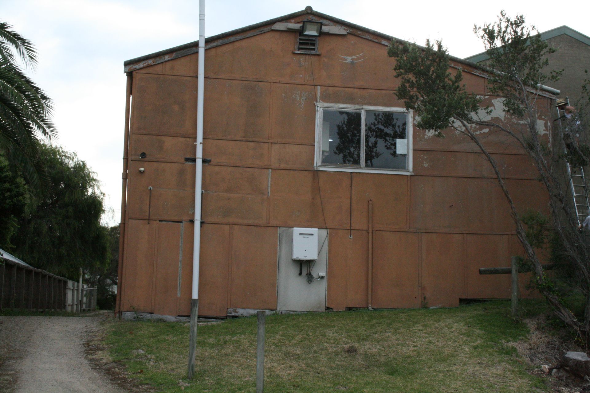 Weathered brown house exterior with a small window, door, and pole in a grassy yard