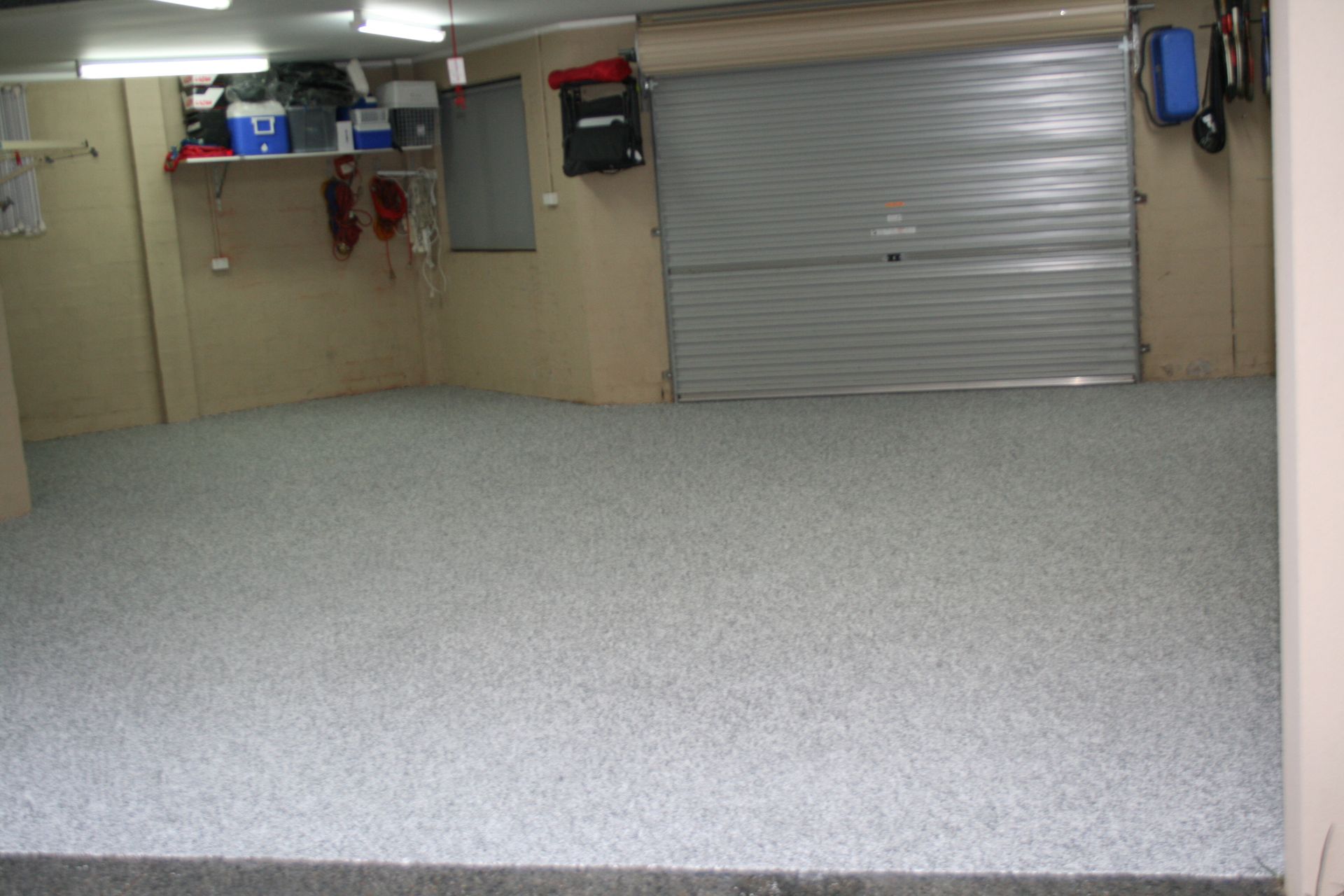 Empty garage with speckled floor, beige walls, and a closed metal roll-up door.