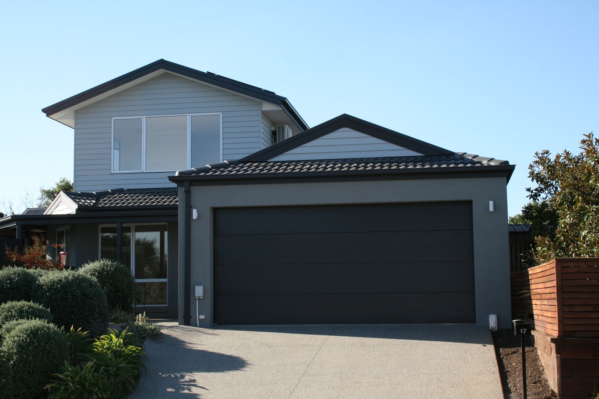 Two-story suburban house with a dark garage door and driveway under a clear blue sky