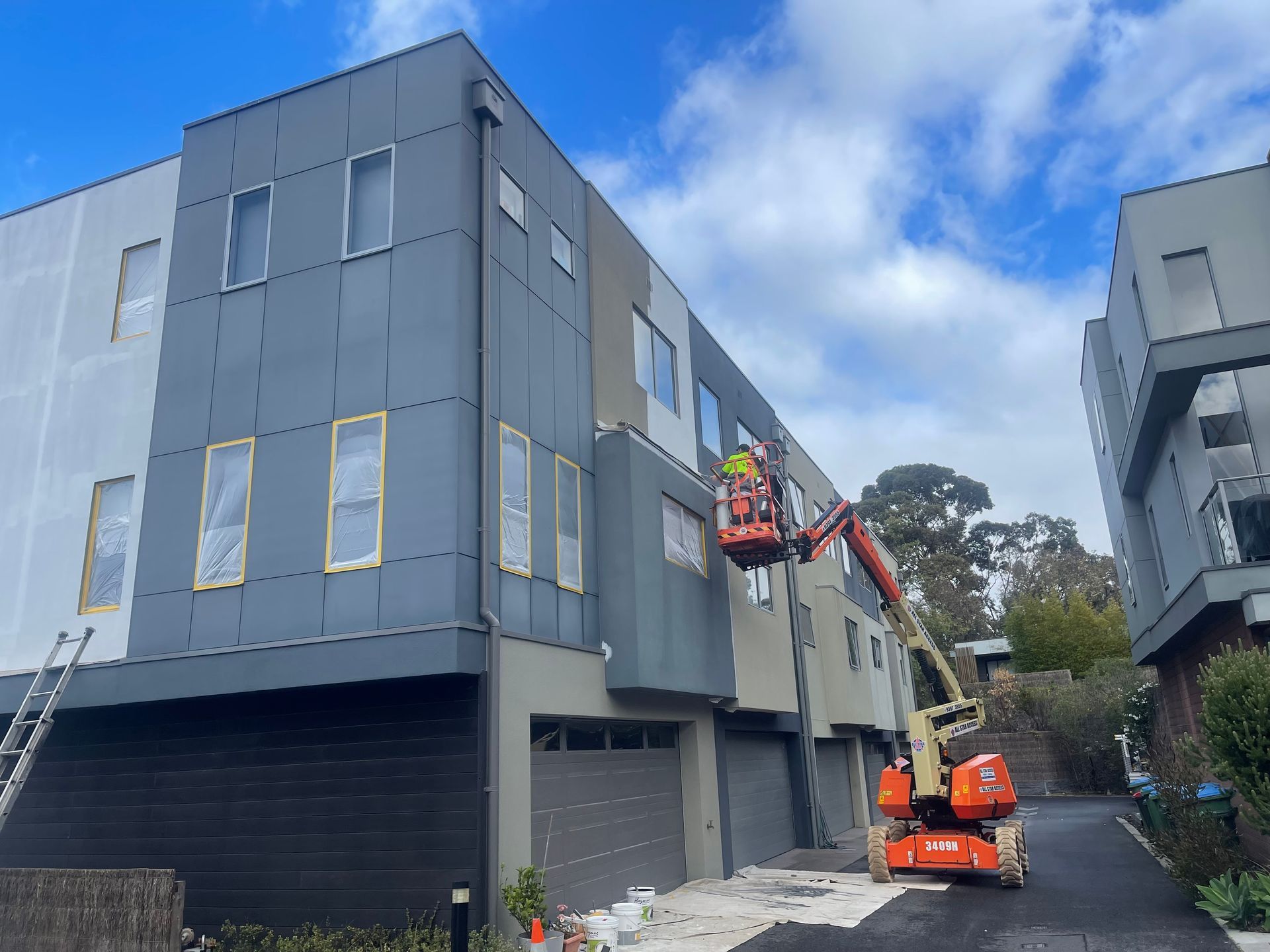 Worker in orange lift inspecting a gray apartment building under construction