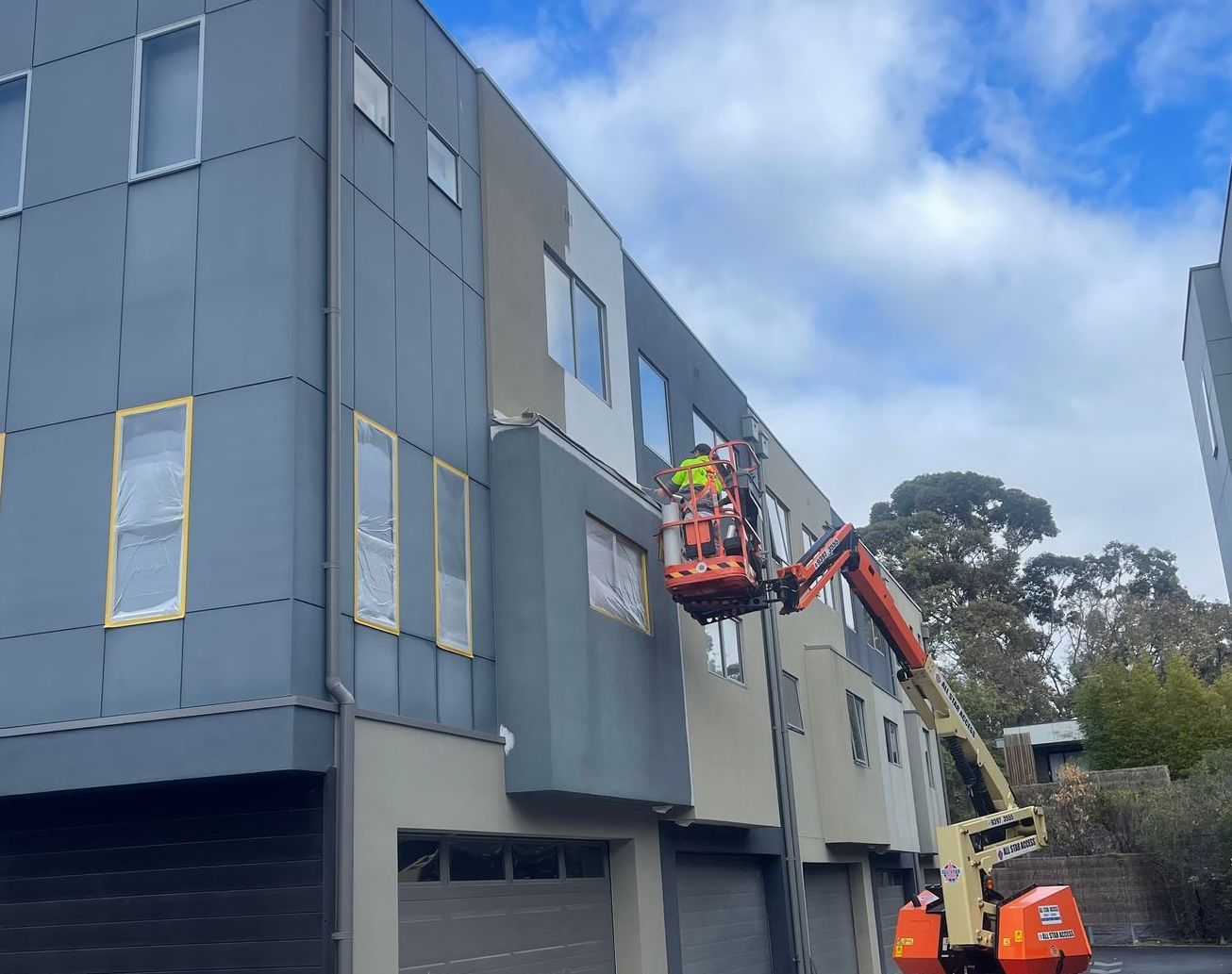 Worker in orange lift repairing gray building facade with cherry picker
