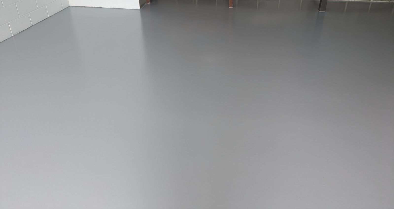 Empty gray floor in a sparse indoor room with a few chairs visible at the top edge