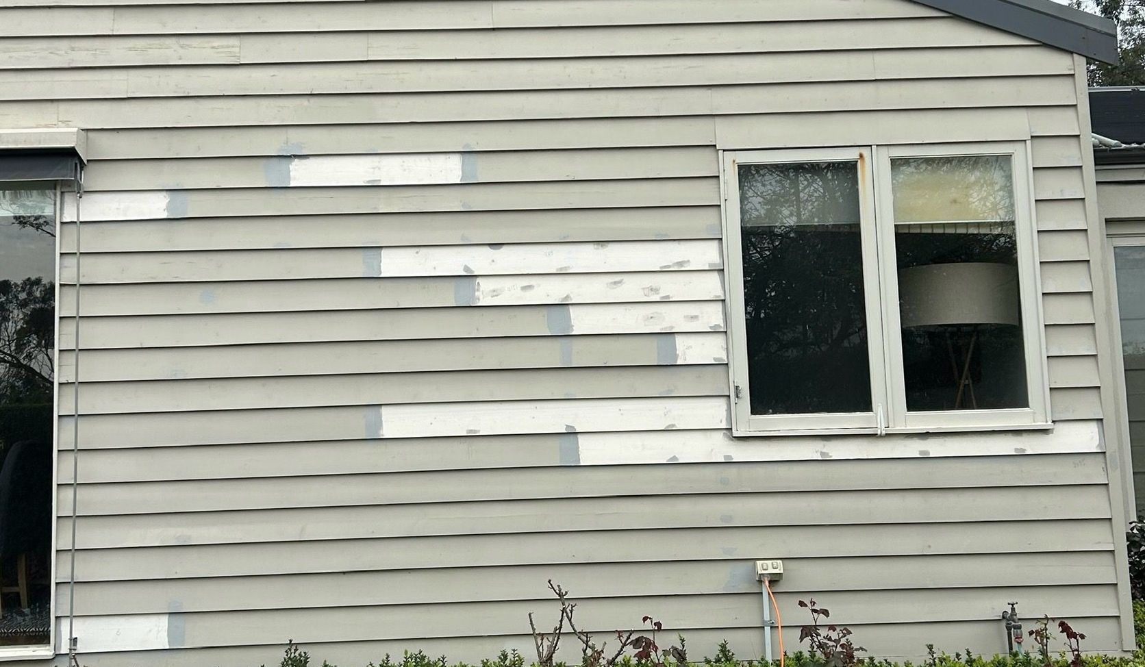 Gray house siding with a double window and white trim, showing several white patch repairs.