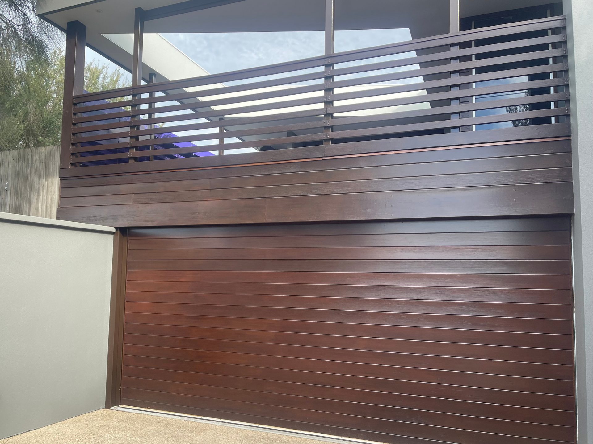 Modern house gate with brown horizontal slats and a matching upper balcony railing