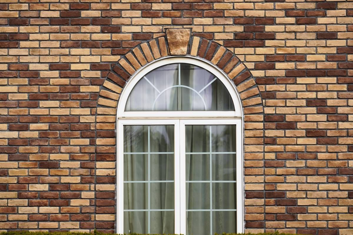 A half-moon window with drapes, shown from the exterior of a multi-colored brick home at Alton Bay Blinds near Hampton, NH