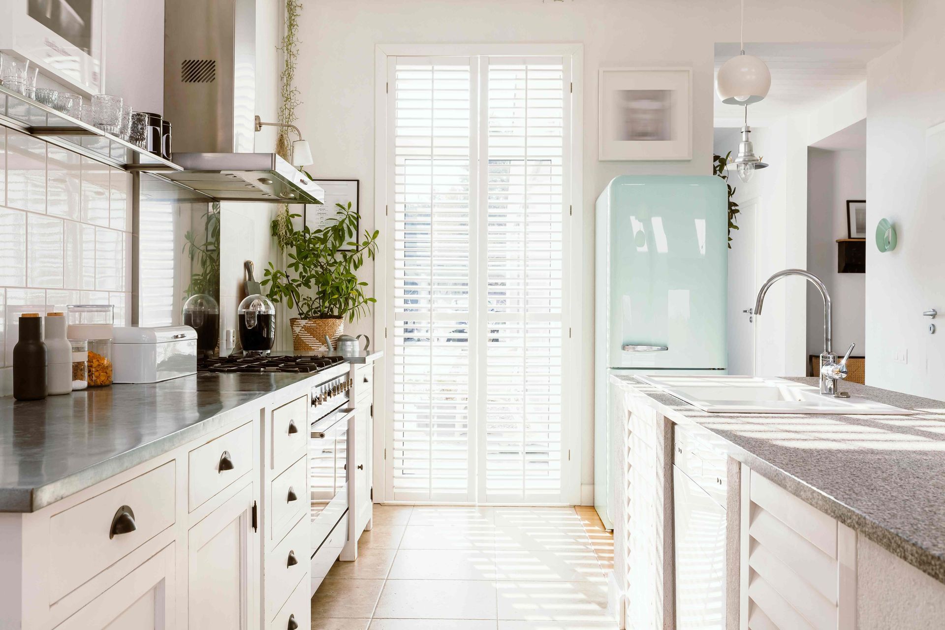 Bright yet cozy kitchen with white cabinets, white window shutters, and a mint blue vintage refriger