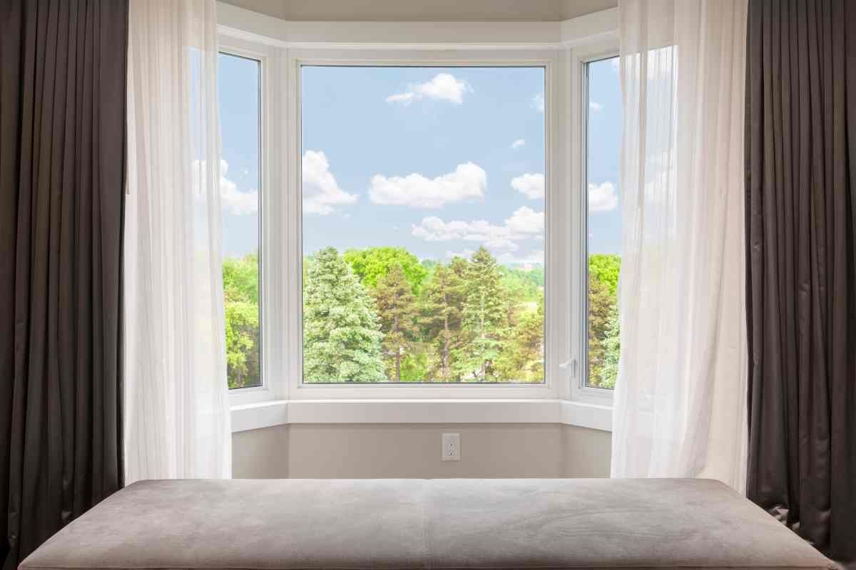 Layered window dressings for a bay window with a view of a blue sky and trees at Alton Bay Blinds near Hampton, NH